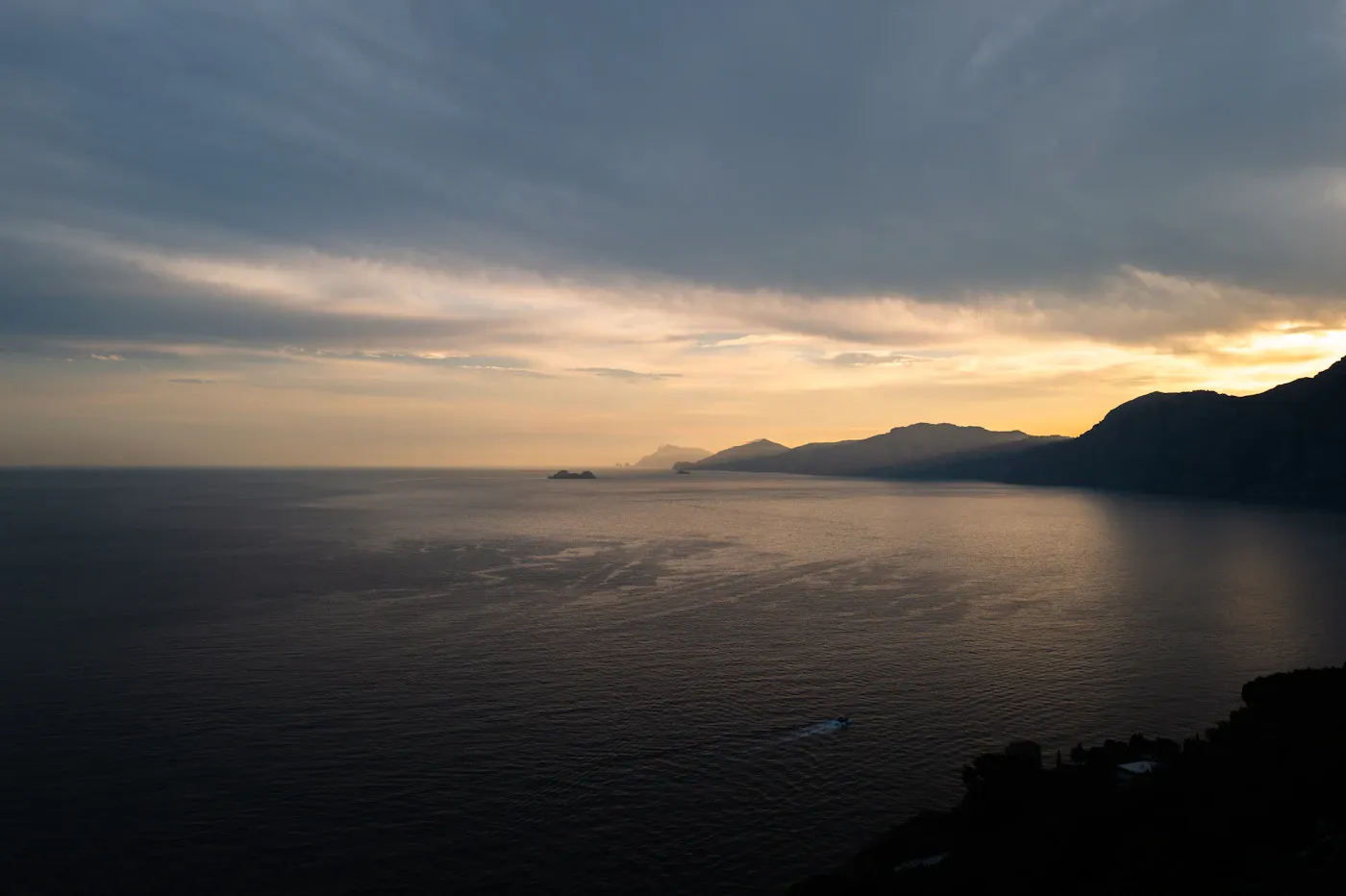 Sunset over the Tyrrhenian Sea, with the mountainous coastline silhouetted beneath clouds in Praiano, Italy.